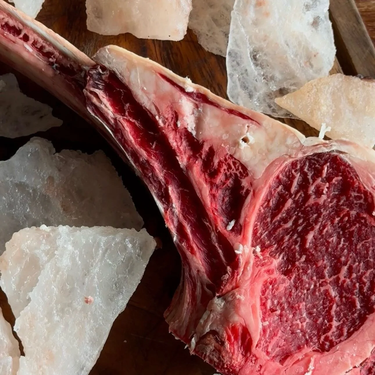 A raw tomahawk steak with rock salt on dark wood
